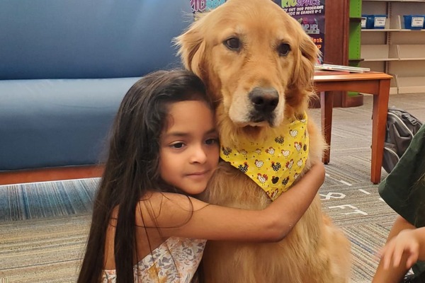 young latina girl with long black hair hugging a large golden retriever with a yellow bandana around its neck