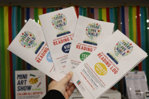 woman's hand holding a fanned out group of Summer Library Challenge Reading logs