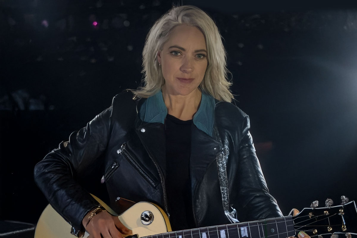 blonde woman wearing leather jacket holding a guitar
