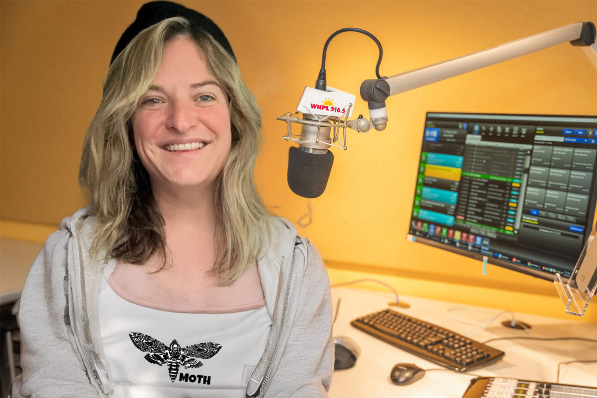 woman smiling at camera in front of microphone with a computer in the background