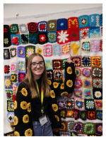 blonde woman with glasses smiling at the camera pointing at a blanket