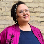 person with brown hair and glasses wearing pink and blue shirt looking at camera
