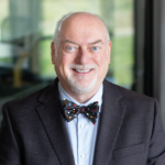 man with with white goatee wearing a dark suit and bowtie smiling at camera