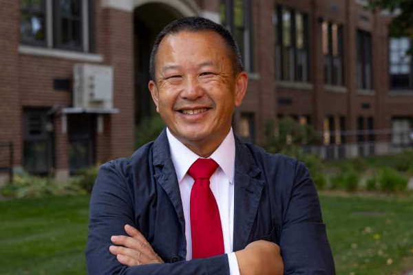 man with dar hair wearing blue suit and red tie smiling at camera