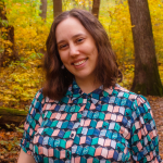 woman with dark hair and a brightly colored shirt standing in a grove of trees