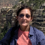 woman wearing dark sunglasses standing in front of a cliffside