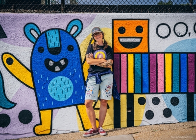 Artist Emily Balsley standing in front of a colorful mural she has painted.