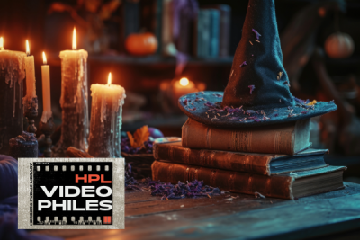 lit and dripping candles next to a stack of books with a witches hat on top