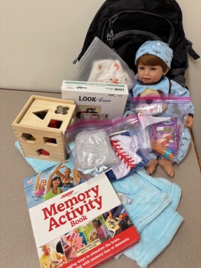 Baby doll, toys, books and activities in front of a backpack