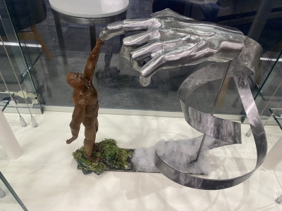 Metal sculpture of a bronze man reaching up to touch giant silver hand