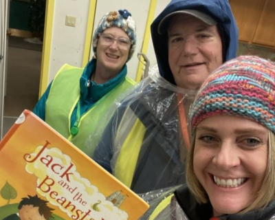 Three adults in warm rain gear. Woman in forefront holds book Jack and the Beanstalk.