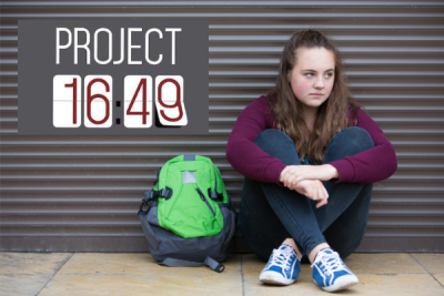 Teen with backpack looking despondent, sitting on sidewalk. 