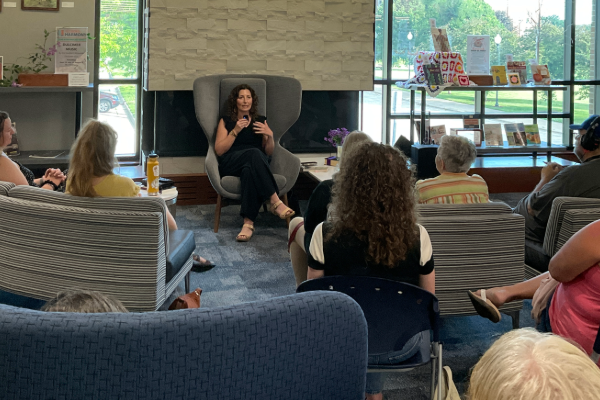 woman sitting in a wingback chair leading a discussion for several onlookers