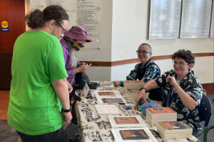 two authors at a table with their books while two onlookers explore their titles