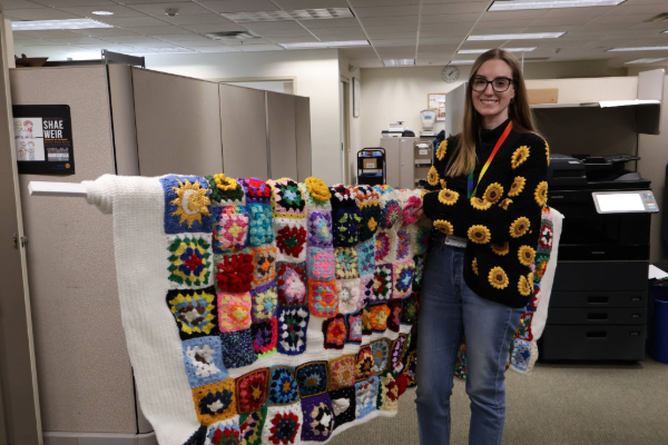 woman with blonde hair and glasses smiling at the camera while holding a rolled up blanket
