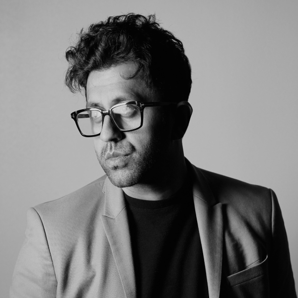 black and white photo of man with dark hari and glasses wearing a suit with no tie