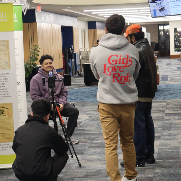 man being interviewed inside a library with others watching