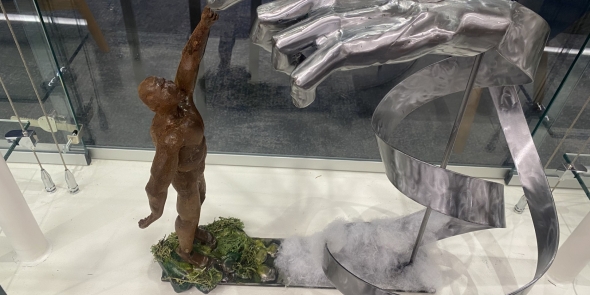 Metal sculpture of a bronze man reaching up to touch giant silver hand