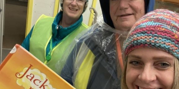 Three adults in warm rain gear. Woman in forefront holds book Jack and the Beanstalk.