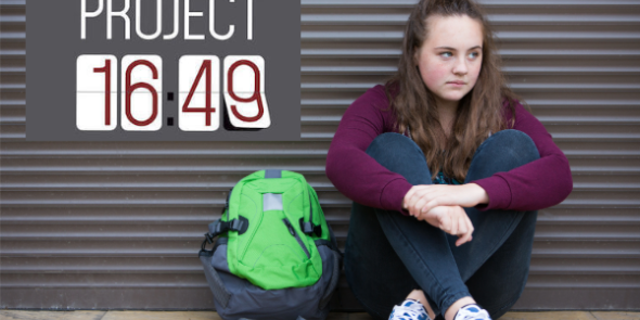 Teen with backpack looking despondent, sitting on sidewalk. 