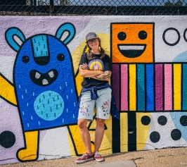 Artist Emily Balsley standing in front of a colorful mural she has painted.