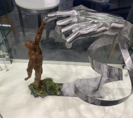 Metal sculpture of a bronze man reaching up to touch giant silver hand