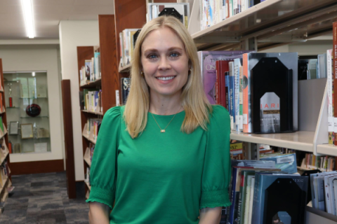Woman with long blonde hair wearing green shirt and smiling at camera