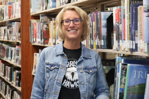 woman with blonde hair wearing jean jacket and glasses smiling at camera