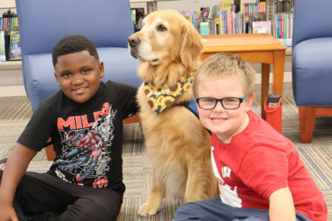 two young boys smiling at the camera sitting next to a golden retriever