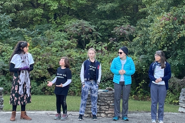 five teen storytellers standing aroun da campfire with trees behind them