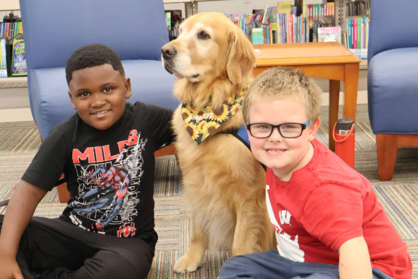 two young boys smiling at the camera sitting next to a golden retriever
