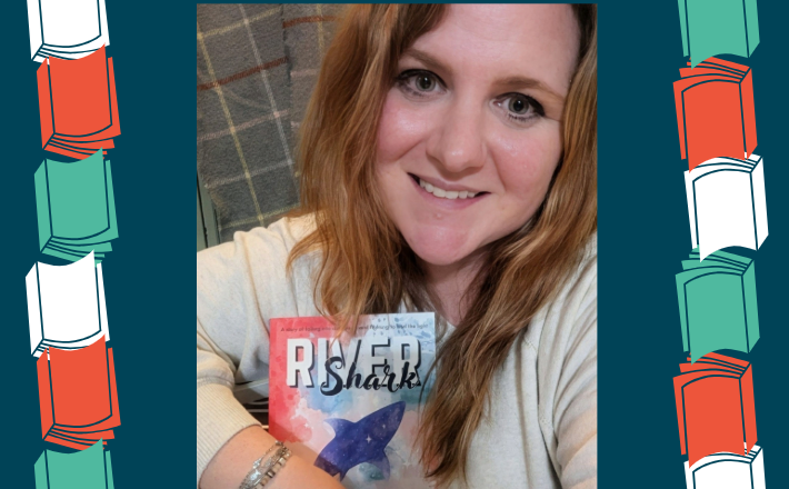 woman with strawberry blonde hair smiling at camera and holding a book