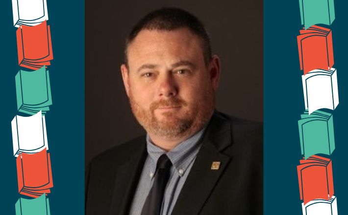 man in dark suit and tie with goatee and brown hair looking at camera